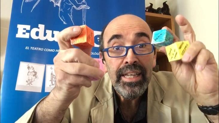 Taller de Educateatro: el formador muestra los dados del juego teatral frente al banner de Educateatro
